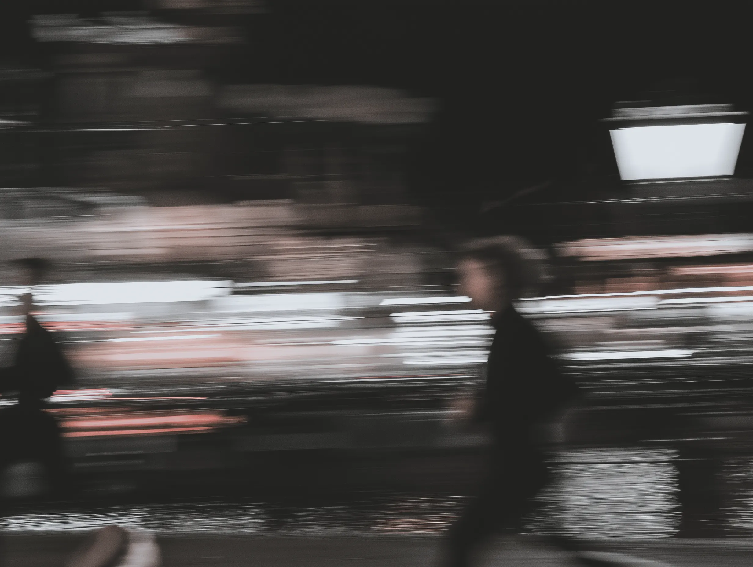 An abstract motion-blurred photograph of silhouettes moving through a city at night, with long horizontal streaks of light.